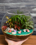 Duckling Pond Terrarium from Planterie hand holded, a miniature glass terrarium with a tiny duckling figurine, moss, pebbles and a pond-like arrangement, perfect for placing on a bright spot away from direct sun or a low light corner in Indian homes and offices