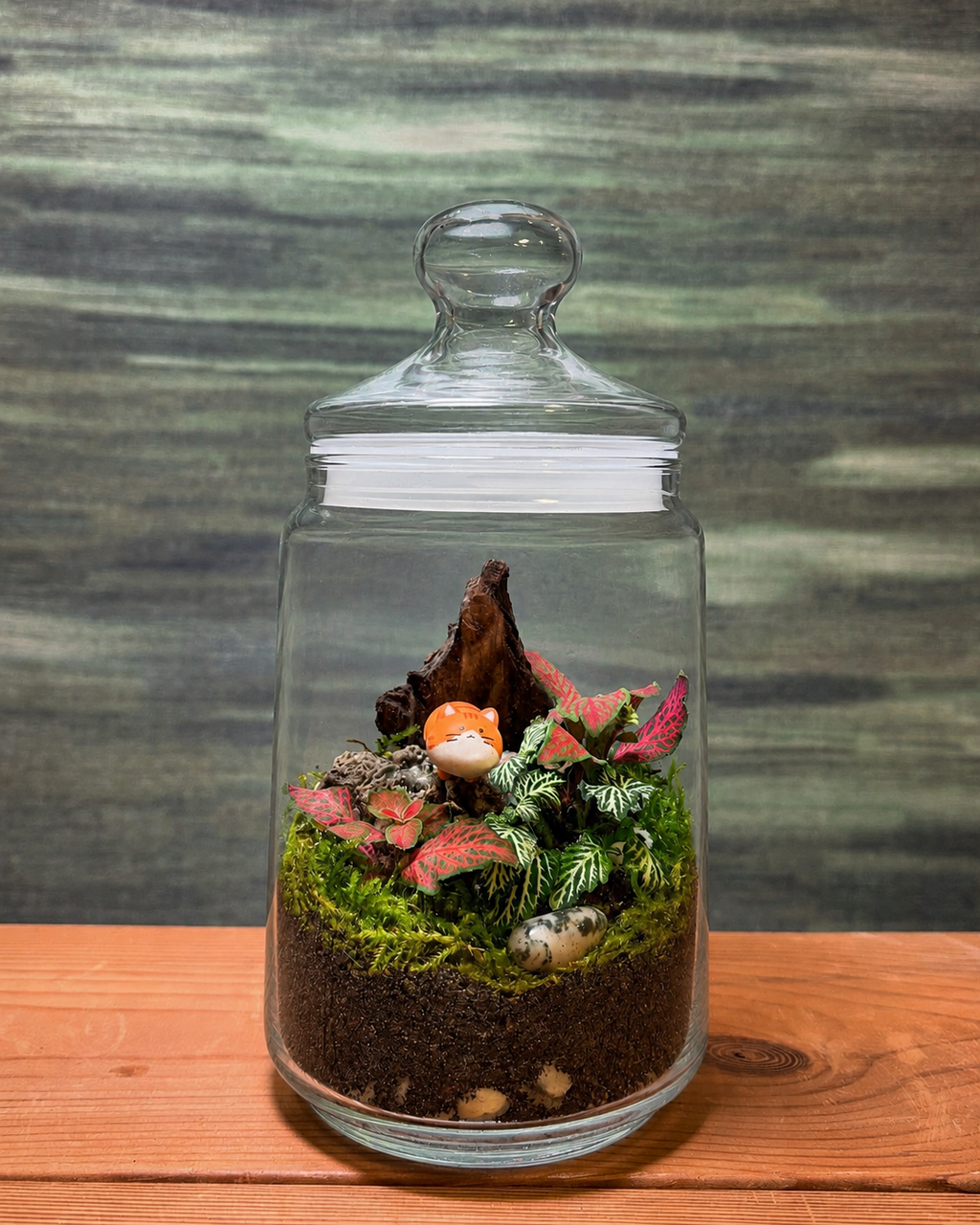 Orange Cat Garden terrarium from Planterie with vibrant green and pink fittonia plants and an adorable orange cat miniature nestled in the greenery, a whimsical glass terrarium in Delhi perfect as plant gifts in Delhi and terrarium gifts India