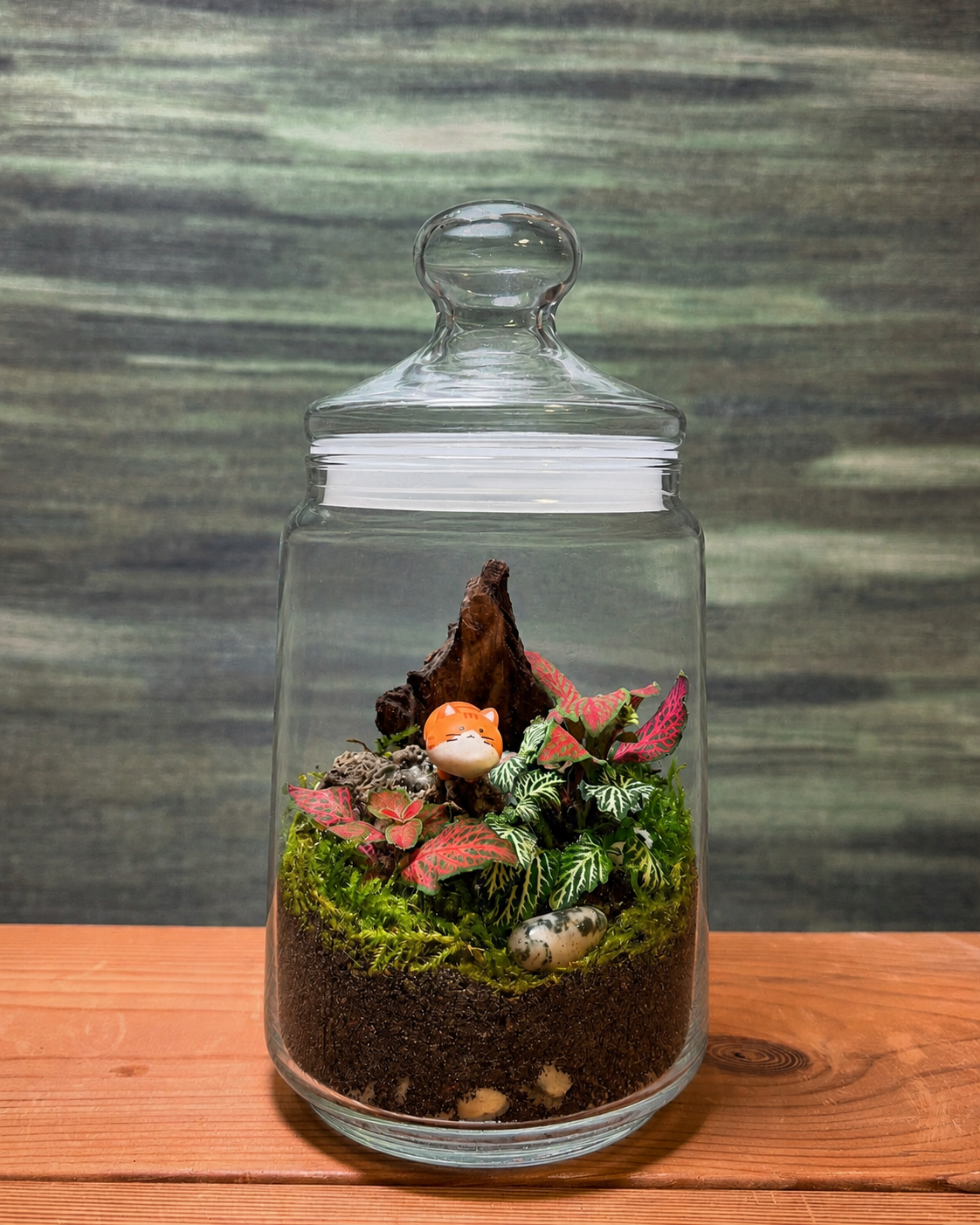 Orange Cat Garden terrarium from Planterie with vibrant green and pink fittonia plants and an adorable orange cat miniature nestled in the greenery, a whimsical glass terrarium in Delhi perfect as plant gifts in Delhi and terrarium gifts India