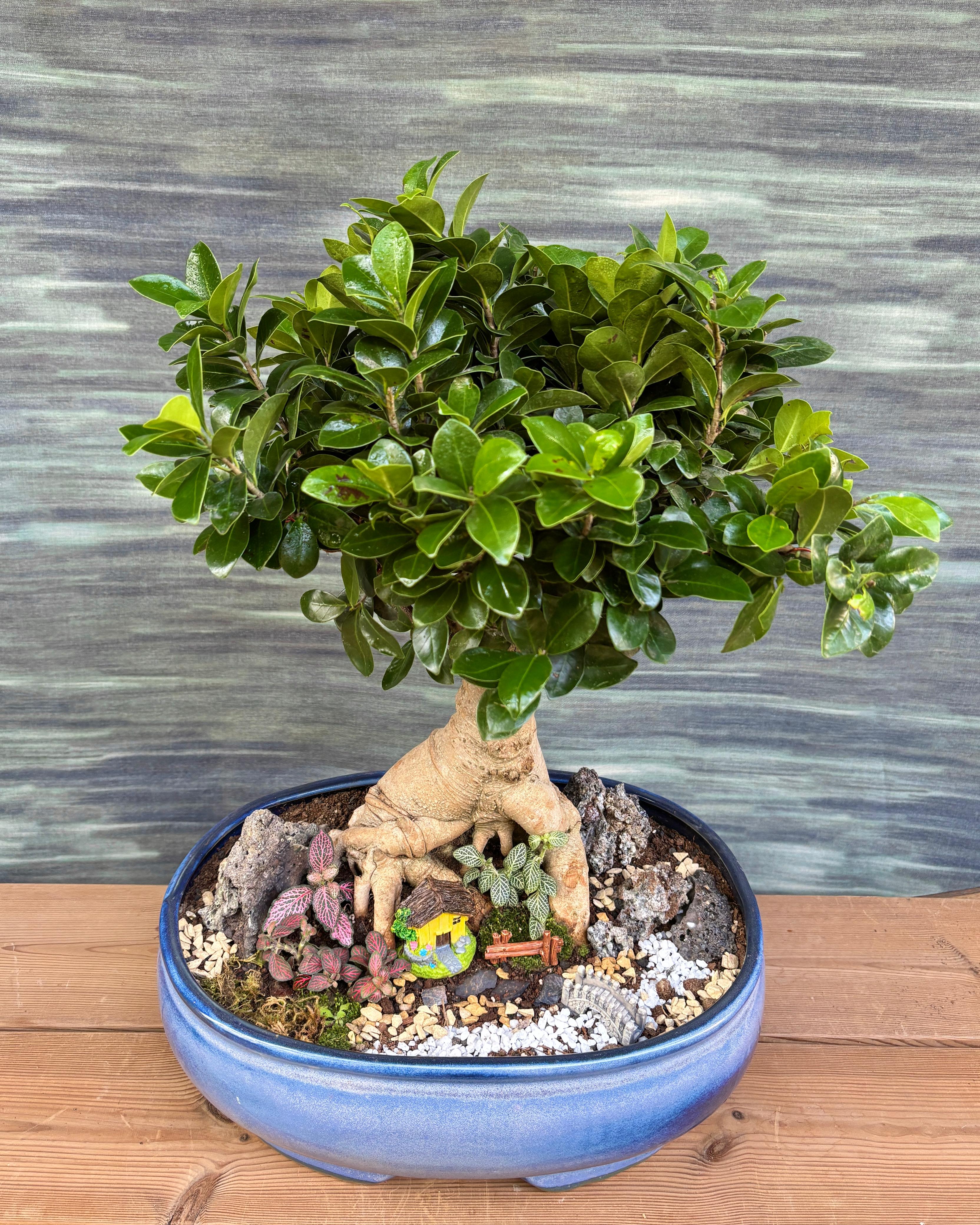 Detail of Riverside Bridge House Bonsai with tiny bridge over a blue river, stones and greenery creating a peaceful scene for Indian homes